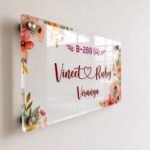 Angled view of floral Vineet and Ruby couple name plate on clear acrylic with standoff mounts