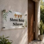 Shree Balaji Nilayam transparent acrylic name plate mounted on a marble wall beside a wooden entrance door