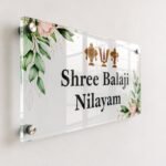 Angled view of transparent Shree Balaji Nilayam acrylic name plate showing glossy finish and standoff mounts